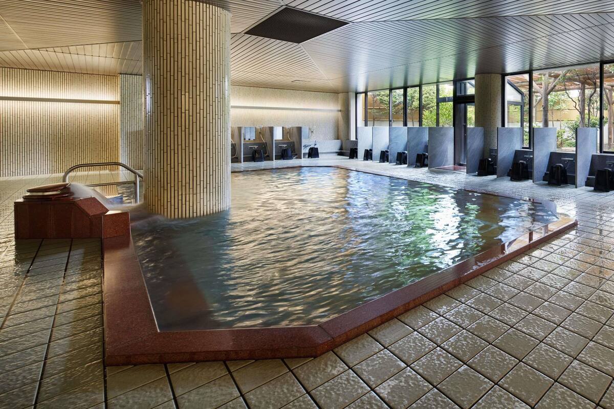Una piscina interior con suelo de baldosas, un pilar de madera y una zona de estar con bancos.