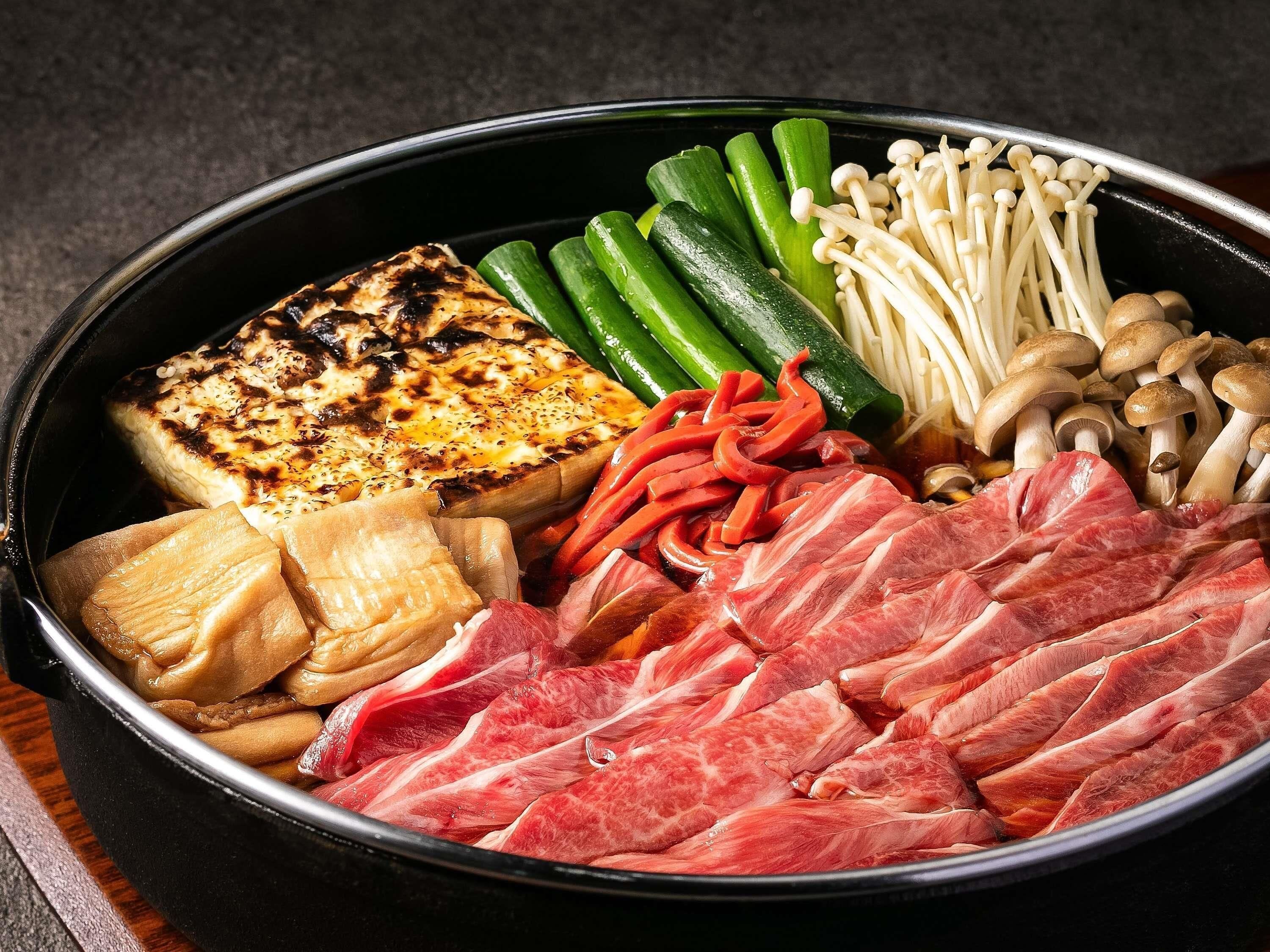 A bowl of assorted food items including grilled tofu, sliced meat, vegetables, and mushrooms.