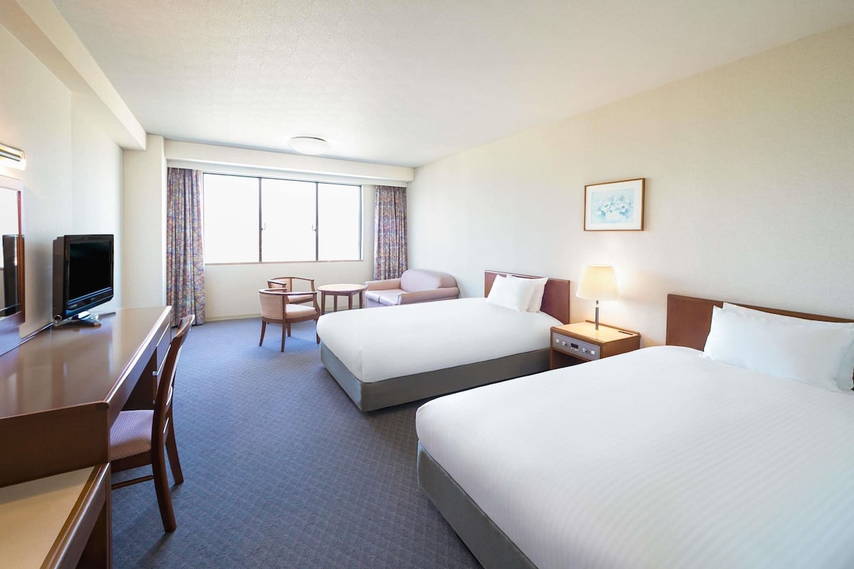A hotel room with two beds, a desk with a television, a chair, and a window with curtains.