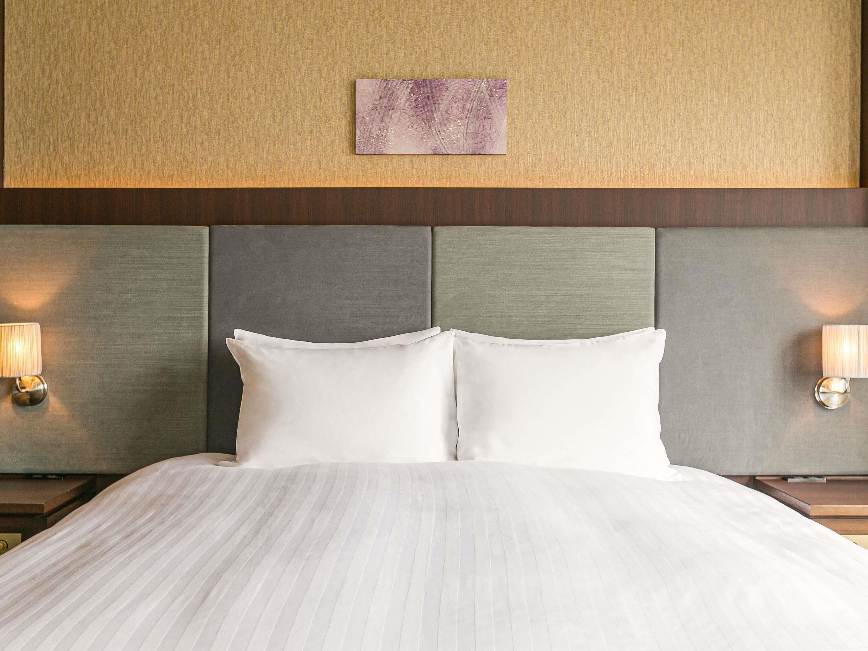A hotel room with a large bed, two bedside lamps, a headboard with a textured panel, and a wall-mounted artwork.