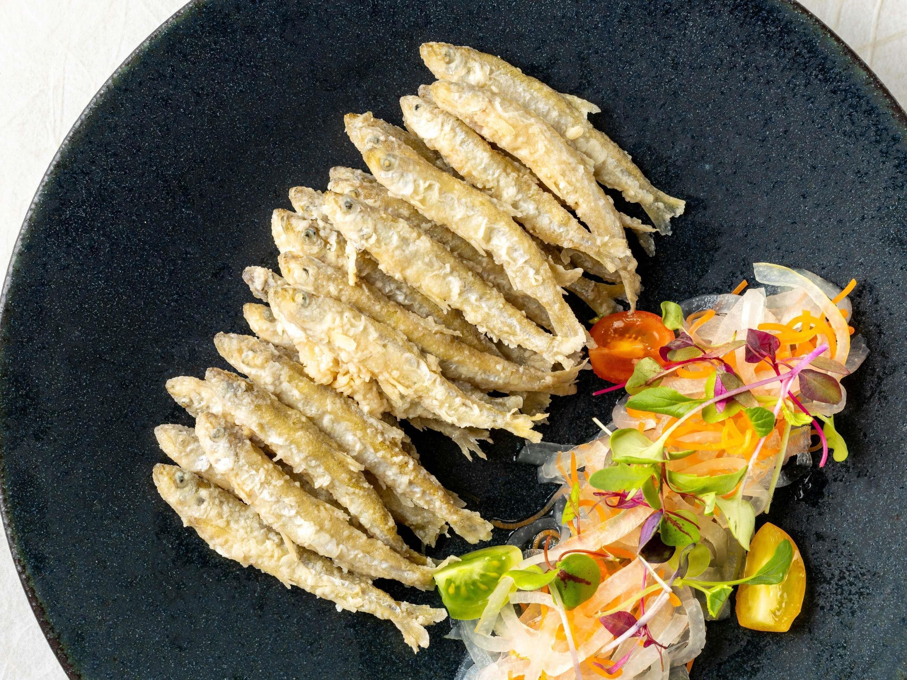 Un plato con pescado frito y una ensalada colorida.
