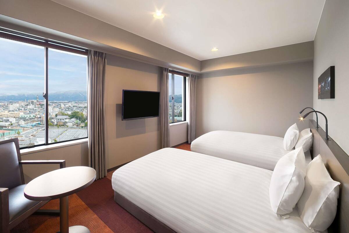 Habitación de hotel con dos camas, televisión, escritorio y vista a la ciudad.