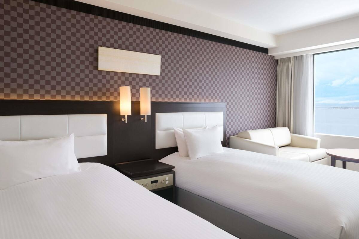 Habitación de hotel con dos camas, un sofá, una mesita y vista al mar.