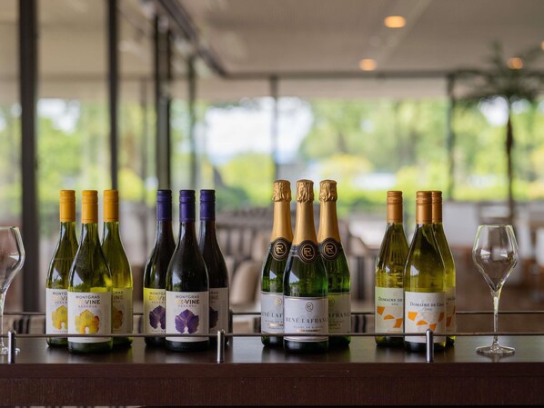 A selection of wine bottles on a bar counter with a view of greenery outside.