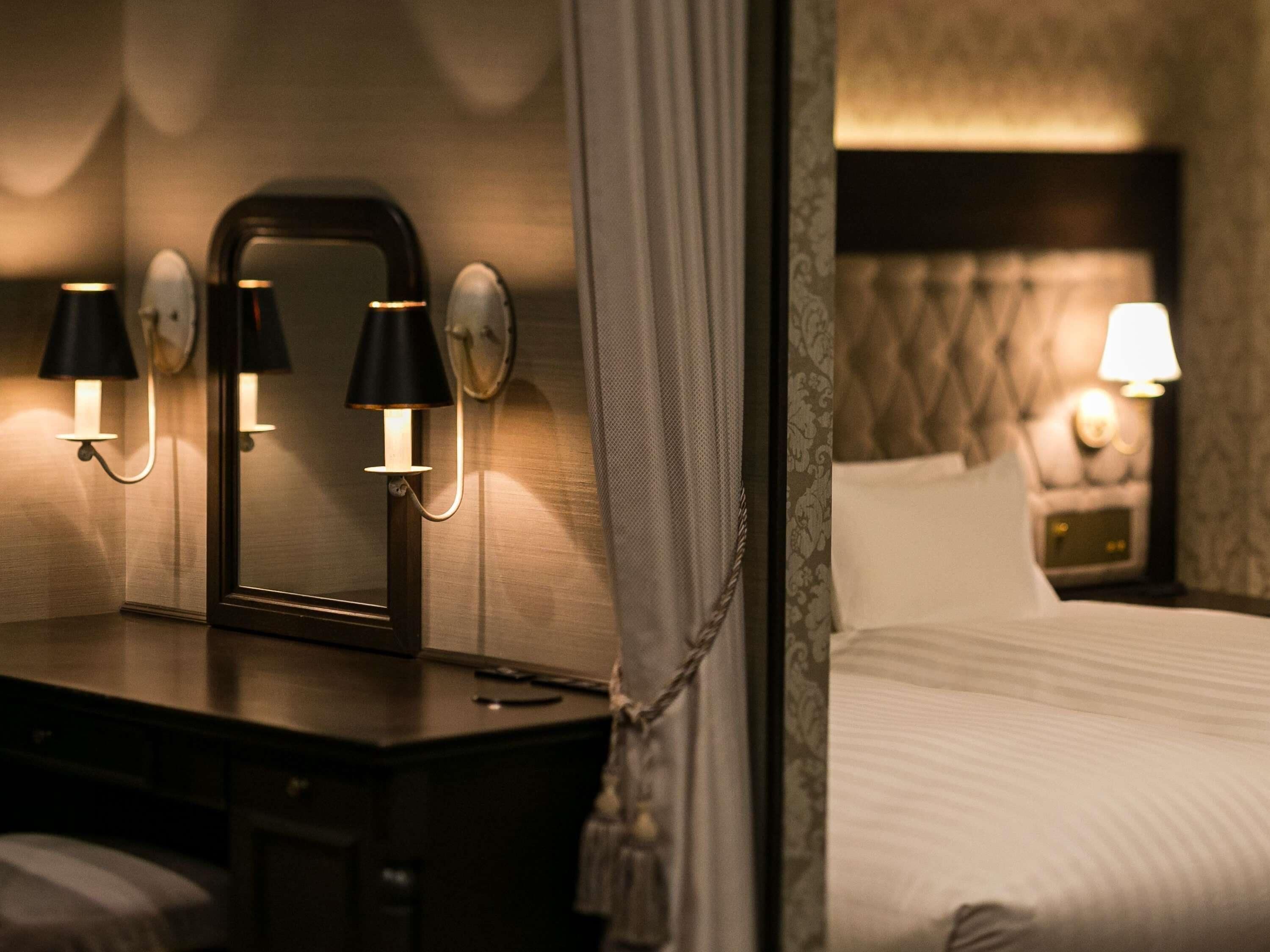 Quarto de hotel com cama, luminárias de cabeceira, espelho e mesa de apoio.