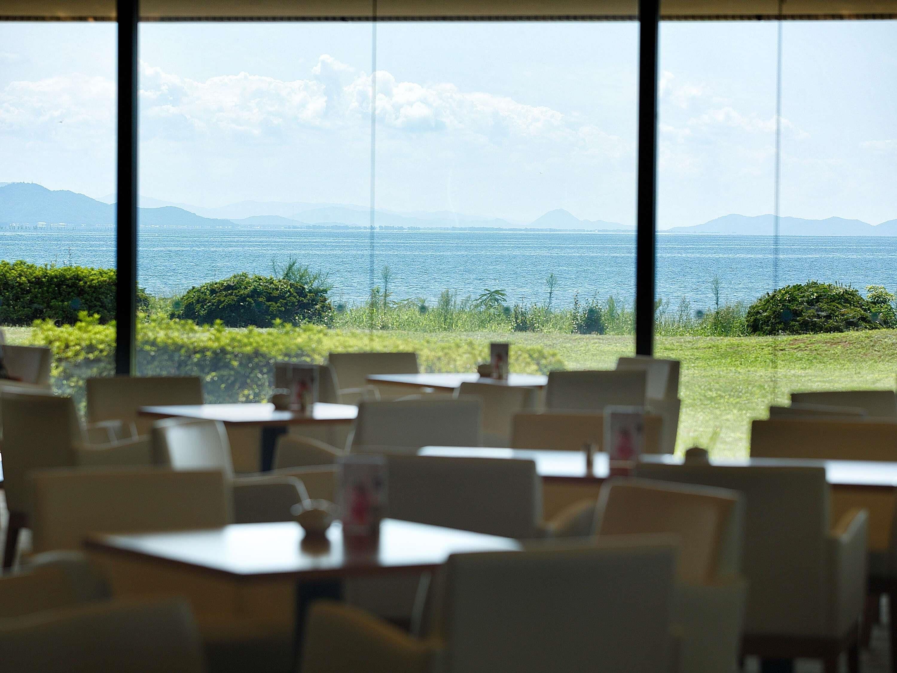 A restaurant with tables and chairs arranged for dining, overlooking a body of water and distant mountains.