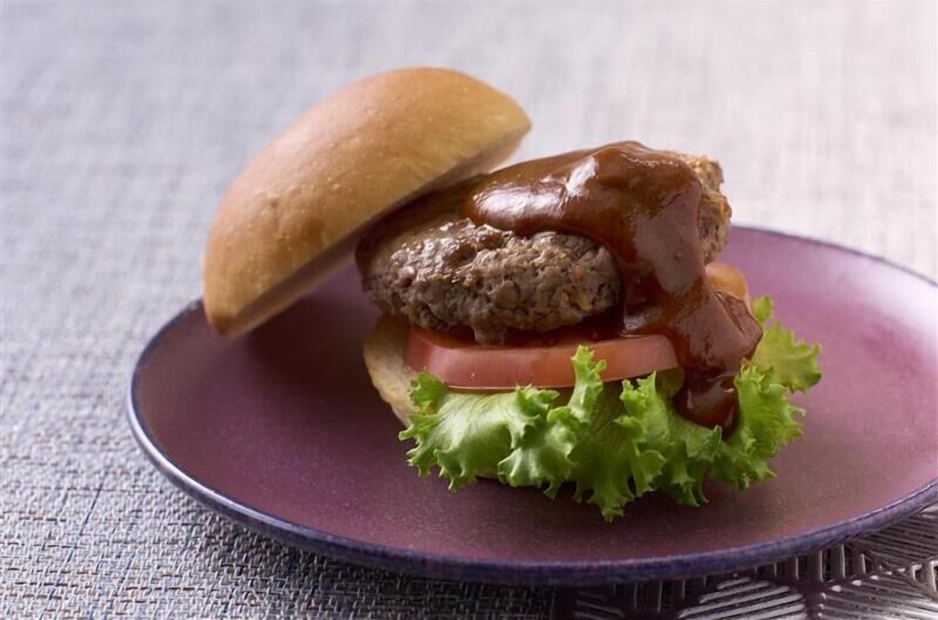 A hamburger with a bun, lettuce, tomato, and a sauce on a purple plate.