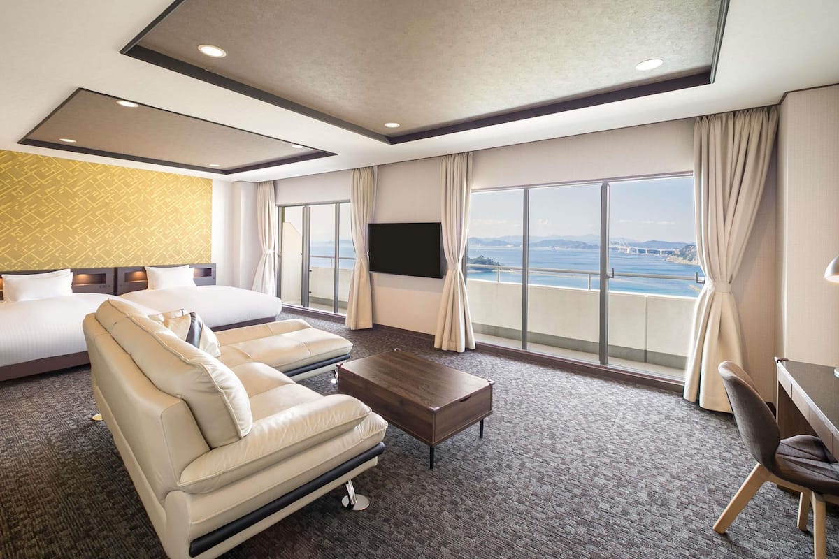 A hotel room with a bed, sofa, TV, and a view of the sea.