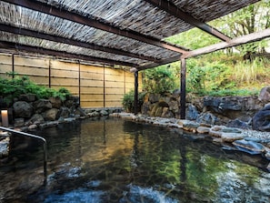 Un onsen japonais traditionnel, agrémenté d’un paravent en bambou, de rochers et d’une terrasse en bois.