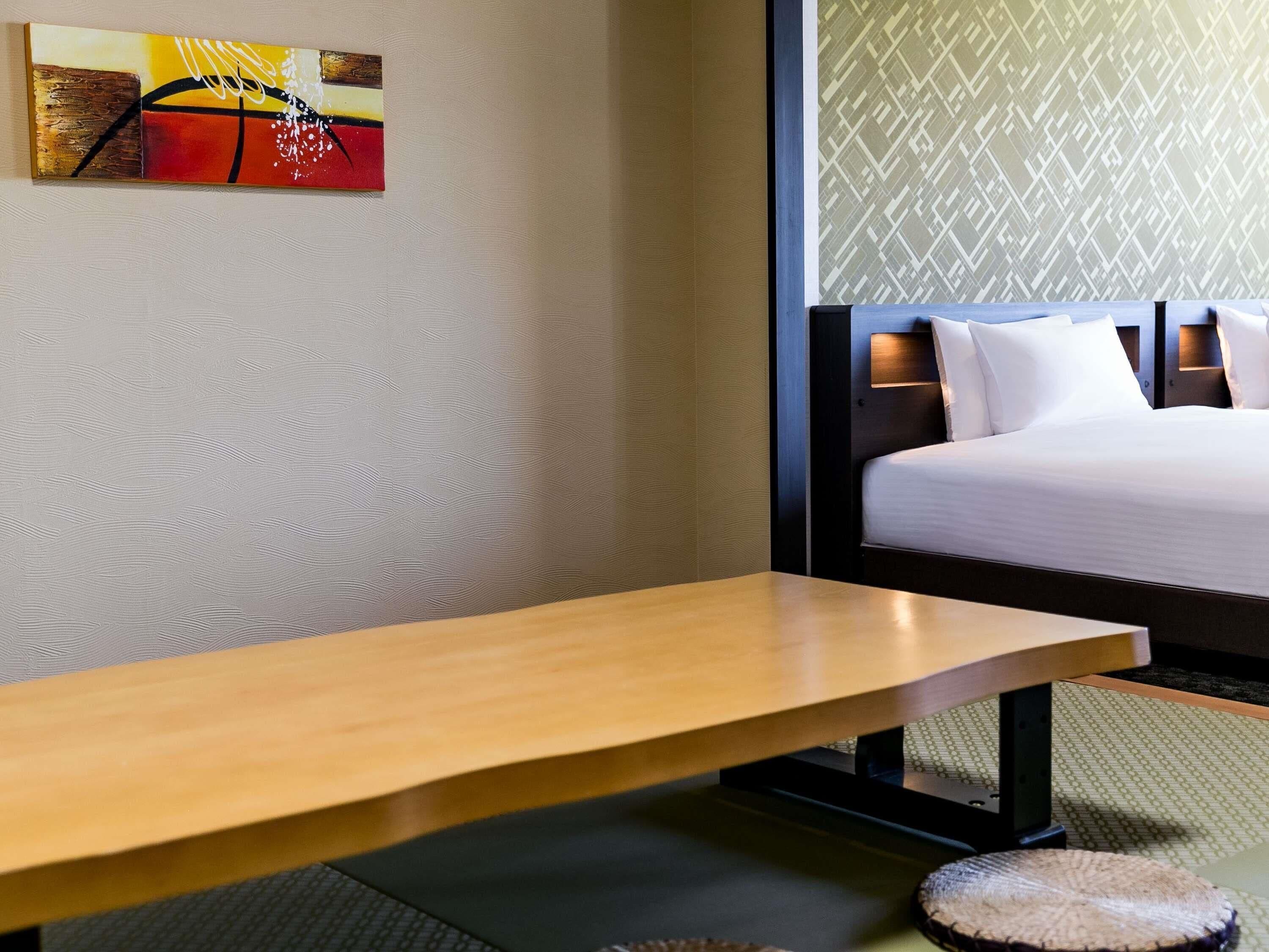 A hotel room with a wooden table, a bed with white bedding, and a patterned wall.