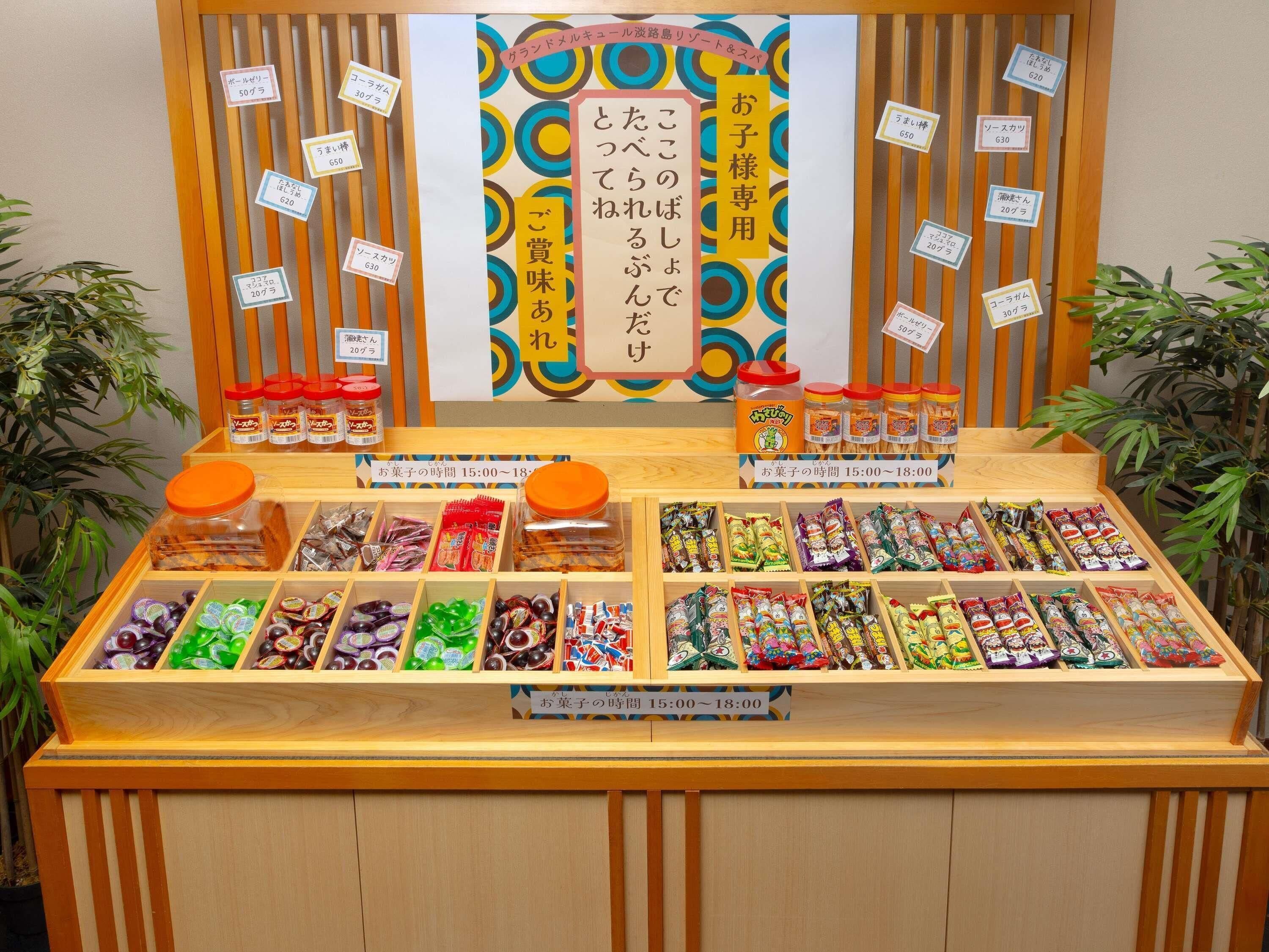 A display of various packaged snacks and condiments with price tags and a wooden counter.