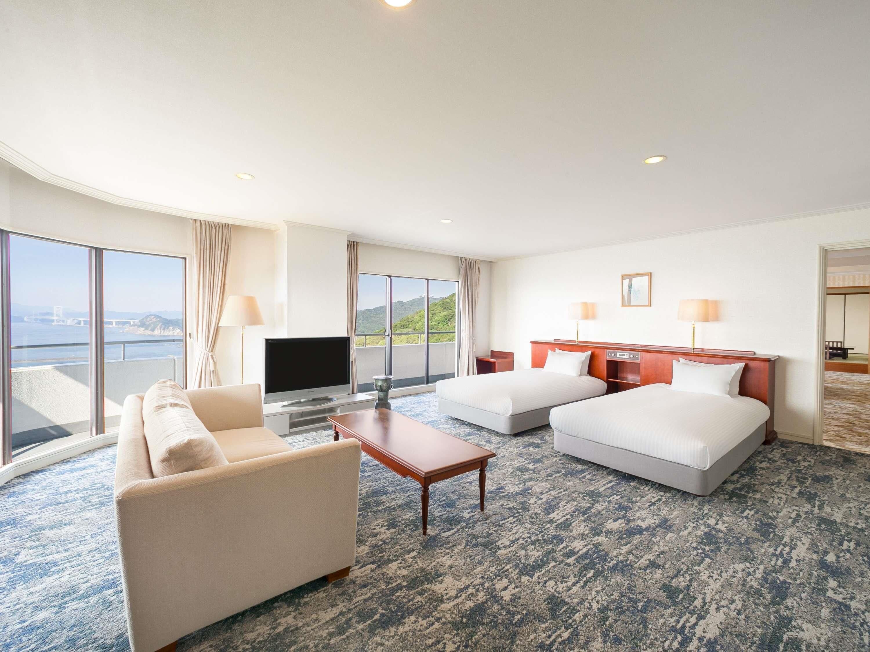 A hotel room with a sofa, two beds, a TV, and a view of a bridge and hills.