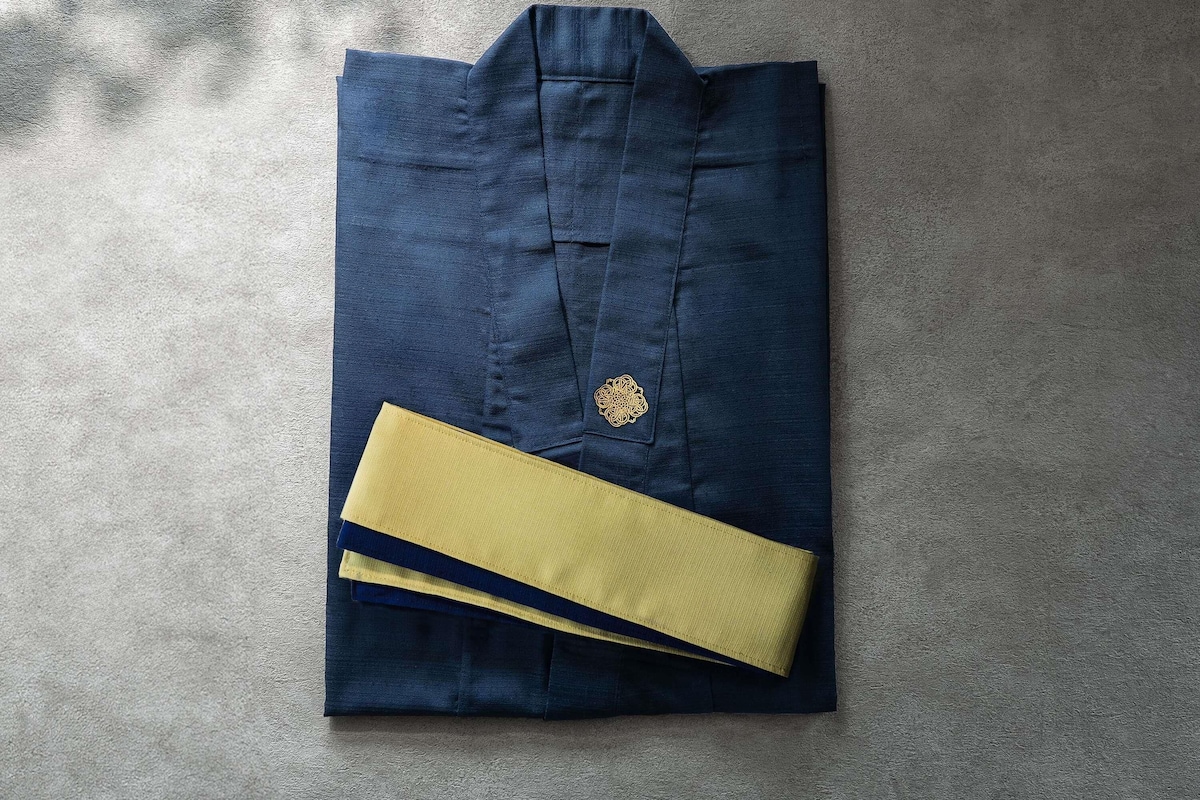 Una camisa azul oscuro doblada con un emblema dorado y un gemelo amarillo sobre una superficie con textura.