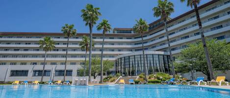A hotel with a swimming pool, palm trees, and a multi-story building.