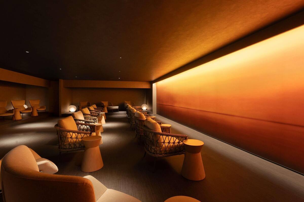 A dimly lit room with rows of wicker chairs and small round tables, suggesting a lounge or waiting area.