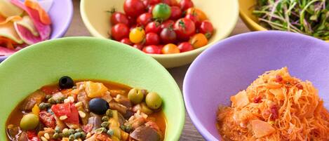 A variety of colorful dishes in bowls, including a vegetable stew, cherry tomatoes, and shredded carrots.