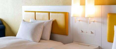 A hotel room with a bed, bedside tables, and wall-mounted lights.