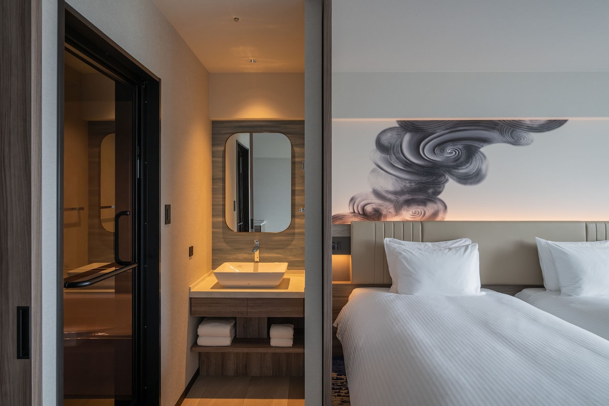 Una habitación de hotel moderna con una cama grande, un baño con lavamanos y espejo, y una pared con un diseño abstracto en espiral.