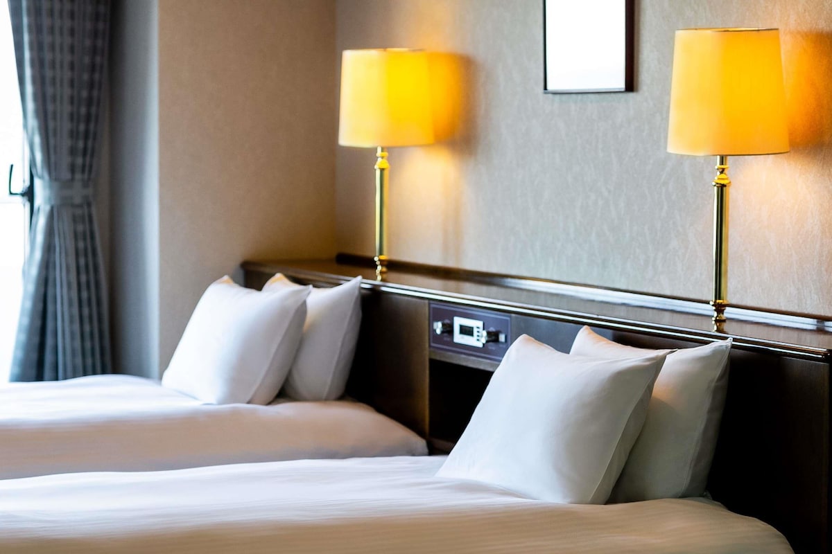 A hotel room with two beds, a control panel, and two lamps.