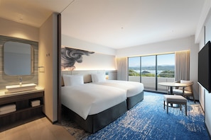 Una habitación de hotel moderna con una cama grande, una zona de estar, un baño con un espejo amplio y vistas a la ciudad.