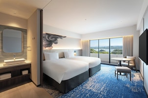 Una habitación de hotel moderna con una cama grande, una zona de estar, un baño con un espejo amplio y vistas a la ciudad.