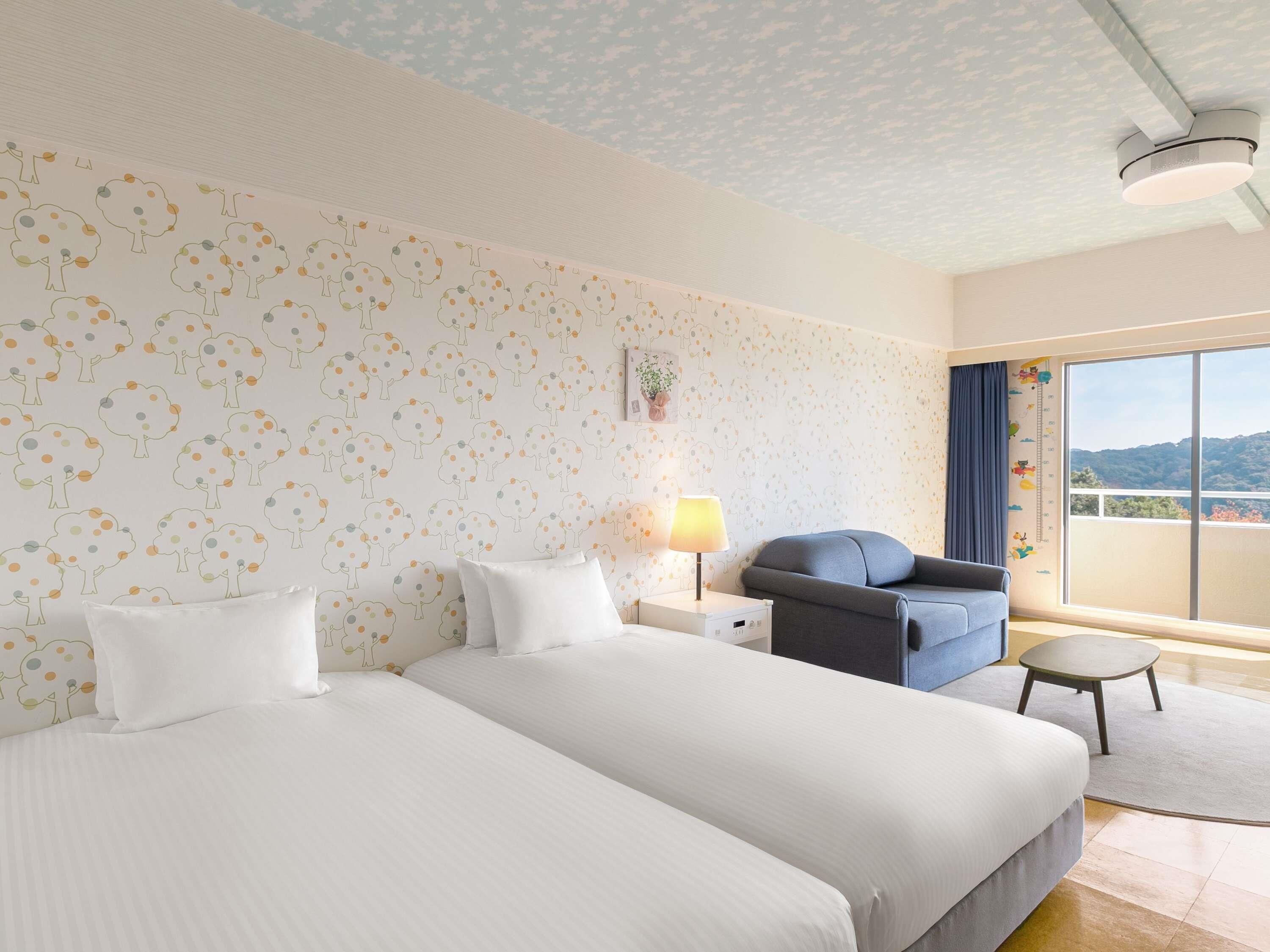 Een hotelkamer met twee bedden, een bureau, een stoel, een raam met uitzicht en een plafond met een decoratief patroon.