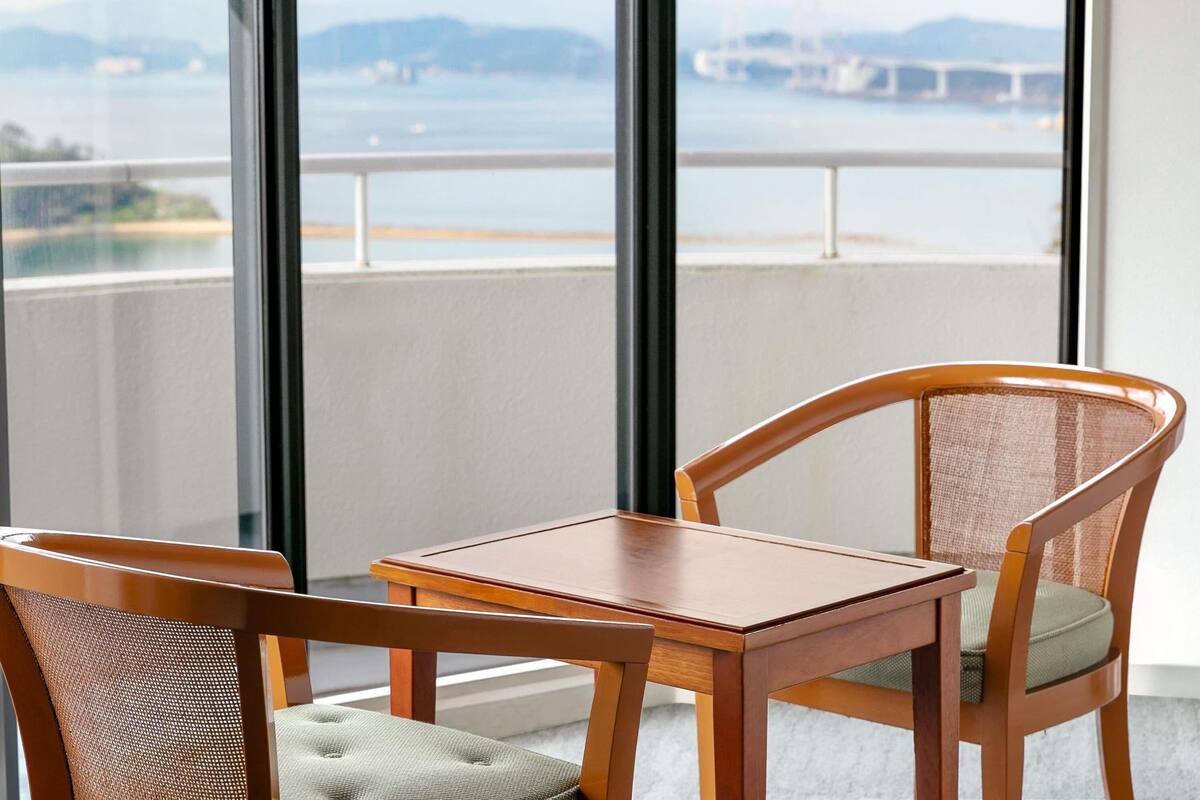 A balcony with a table and two chairs, overlooking a body of water and a bridge.