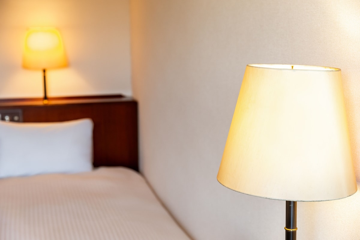 Una habitación de hotel con cama, lámpara de noche y mesita.