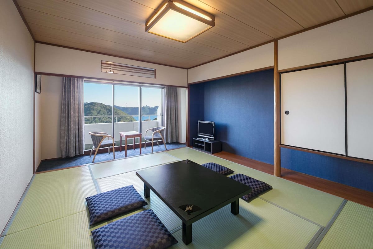 A traditional Japanese room with tatami flooring, a low table, a TV, and a sliding door.