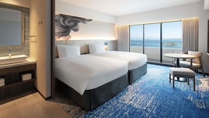 Habitación de hotel con una cama grande, un escritorio, una silla, un baño con espejo y vista al mar.