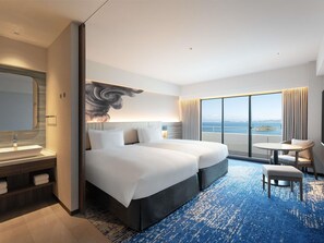 A hotel room with a large bed, a desk, a chair, a bathroom with a mirror, and a view of the sea.
