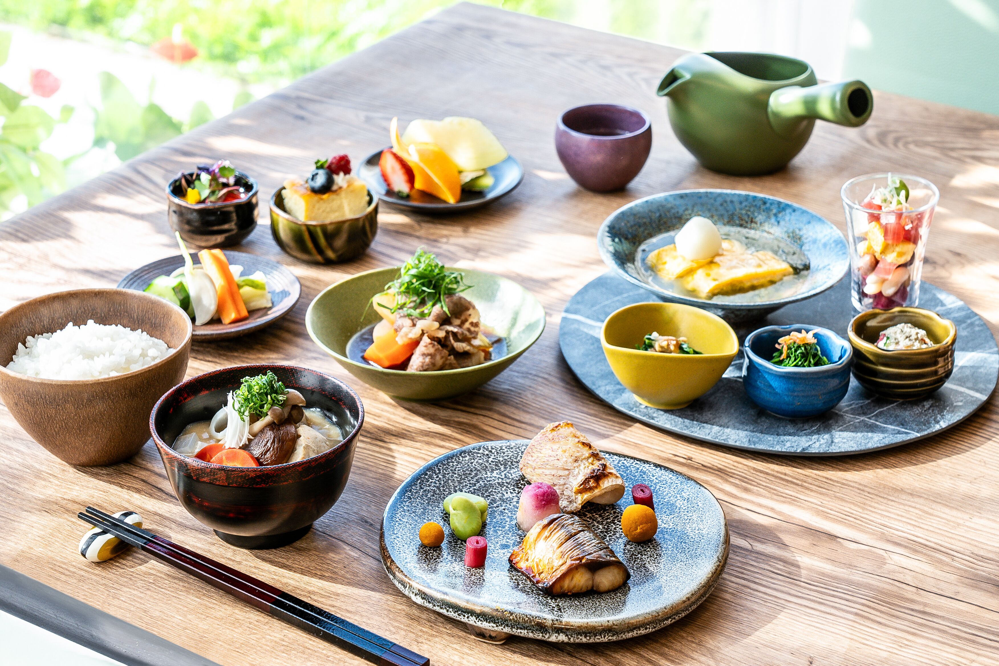 A wooden table with various dishes and bowls of food, including rice, vegetables, and meat.