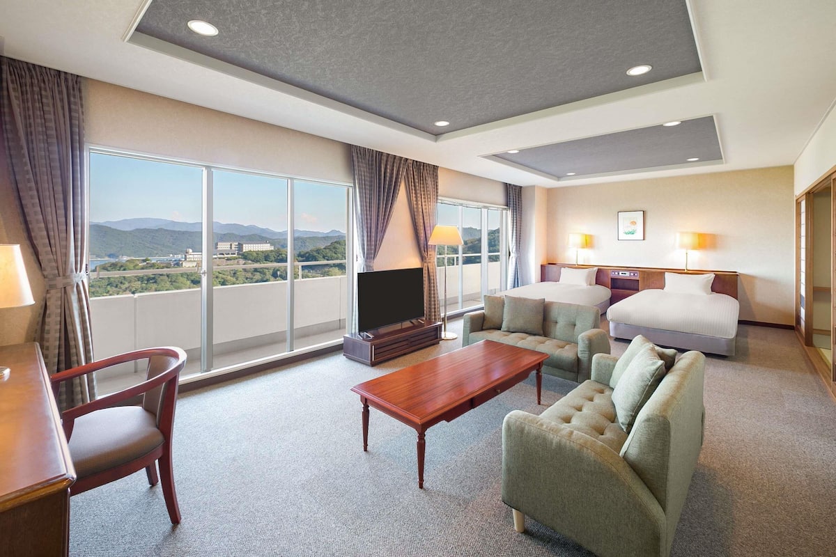 A hotel room with a large bed, a sofa, a TV, and a balcony with a view of the mountains.