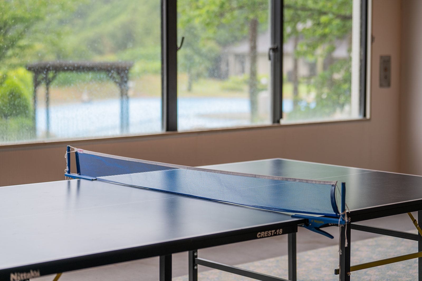 A table tennis table with a net in a room with large windows.