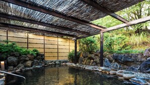 Un onsen japonés tradicional con una celosía de bambú, paredes de piedra y una piscina de agua cristalina.