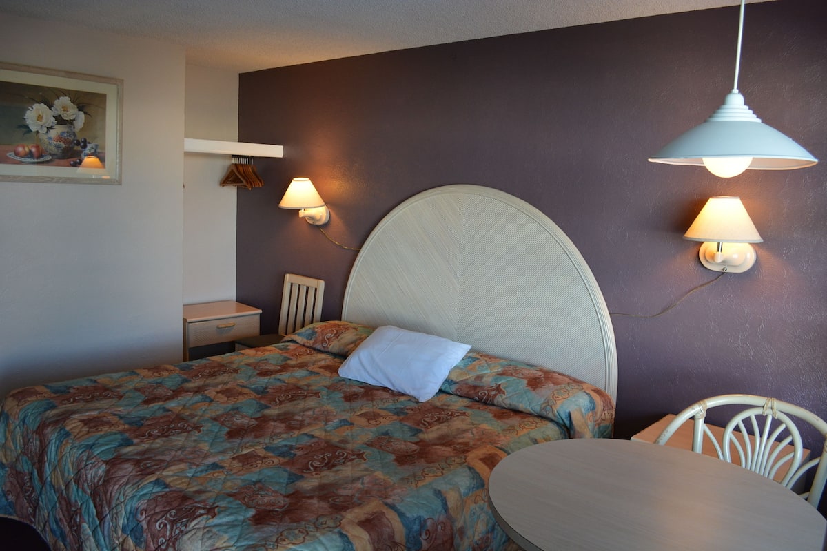 A bedroom with a large bed, a bedside table, a chair, and two wall-mounted lamps.