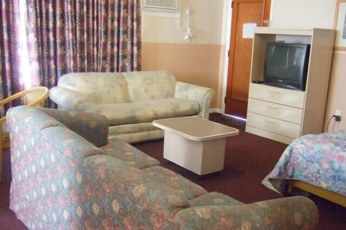 A room with a sofa, a small table, a television, and a bed.