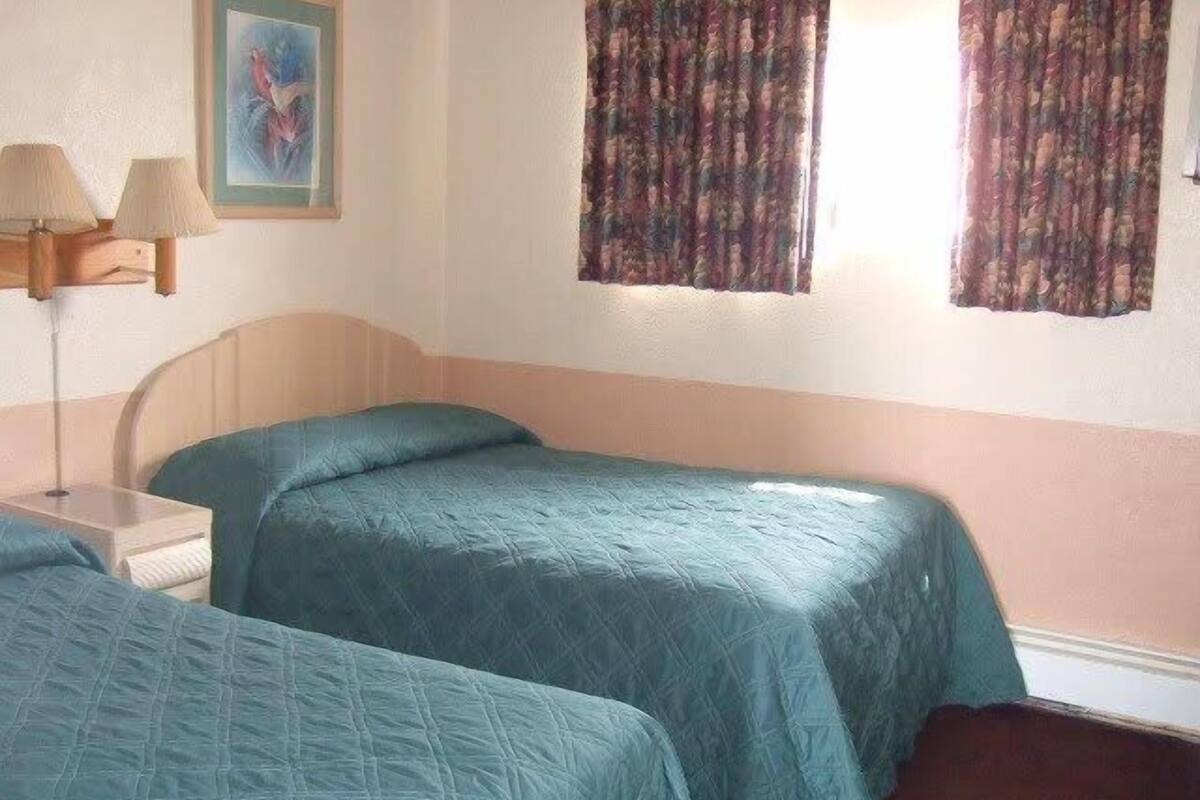 A room with two beds, a nightstand, a lamp, and a painting on the wall.