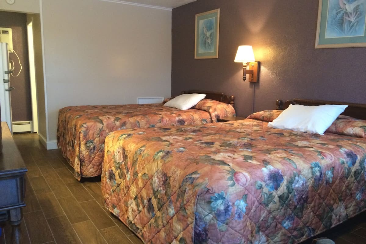A hotel room with two beds, a nightstand, a lamp, and a painting on the wall.