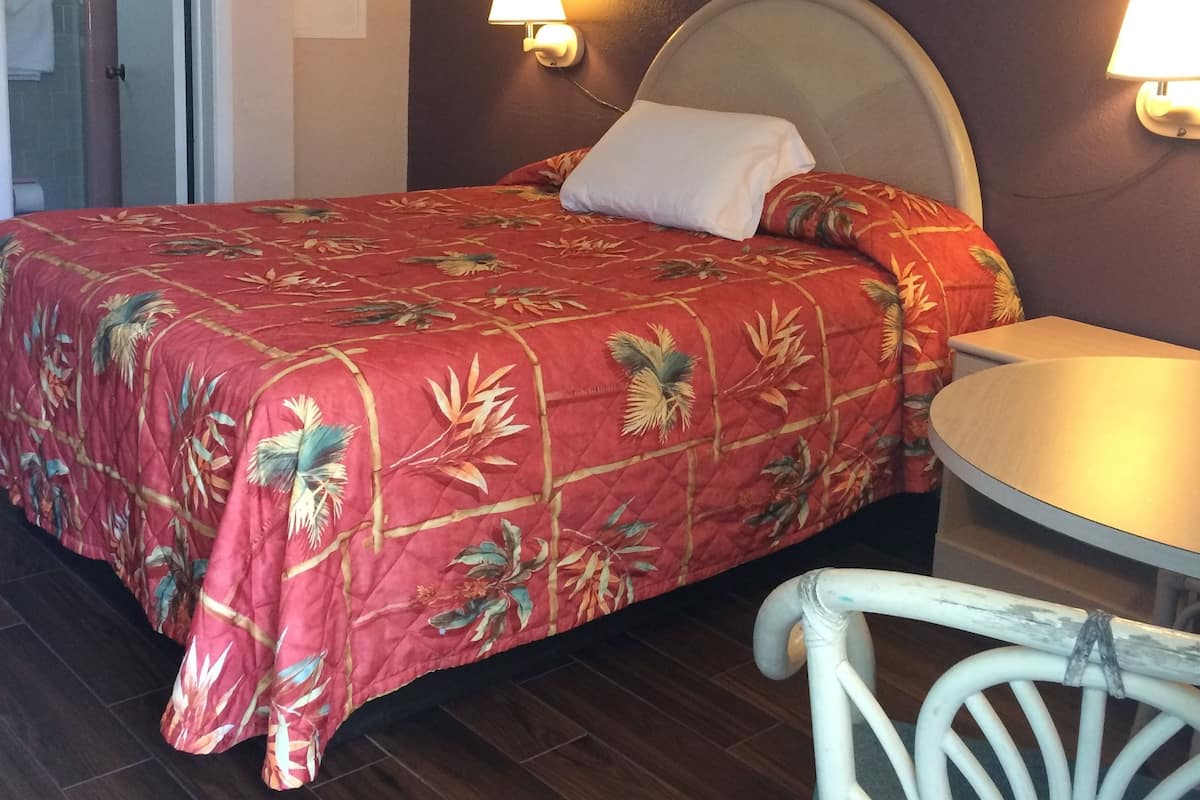 A hotel room with a bed, a chair, a table, and two wall-mounted lamps.