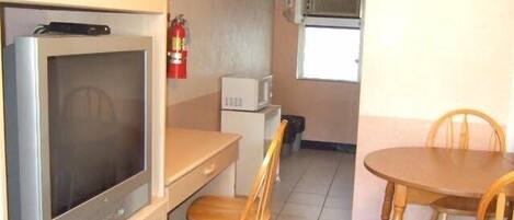 A compact room with a kitchenette, a dining table with chairs, a television, and a microwave.