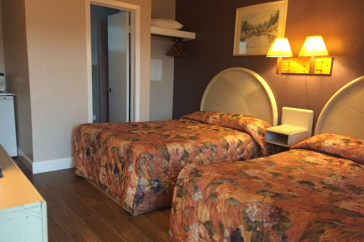 A room with two beds, a small table, a lamp, and a painting on the wall.