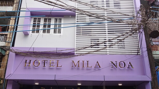 Das Hotel Mila Noa mit violett angemalter Fassade, einem gut sichtbaren Eingang und einer Panasonic-Klimaanlage vor der Fassade.