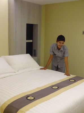 A neatly made bed with a decorative bedspread, a plain wall, and a door in the background.