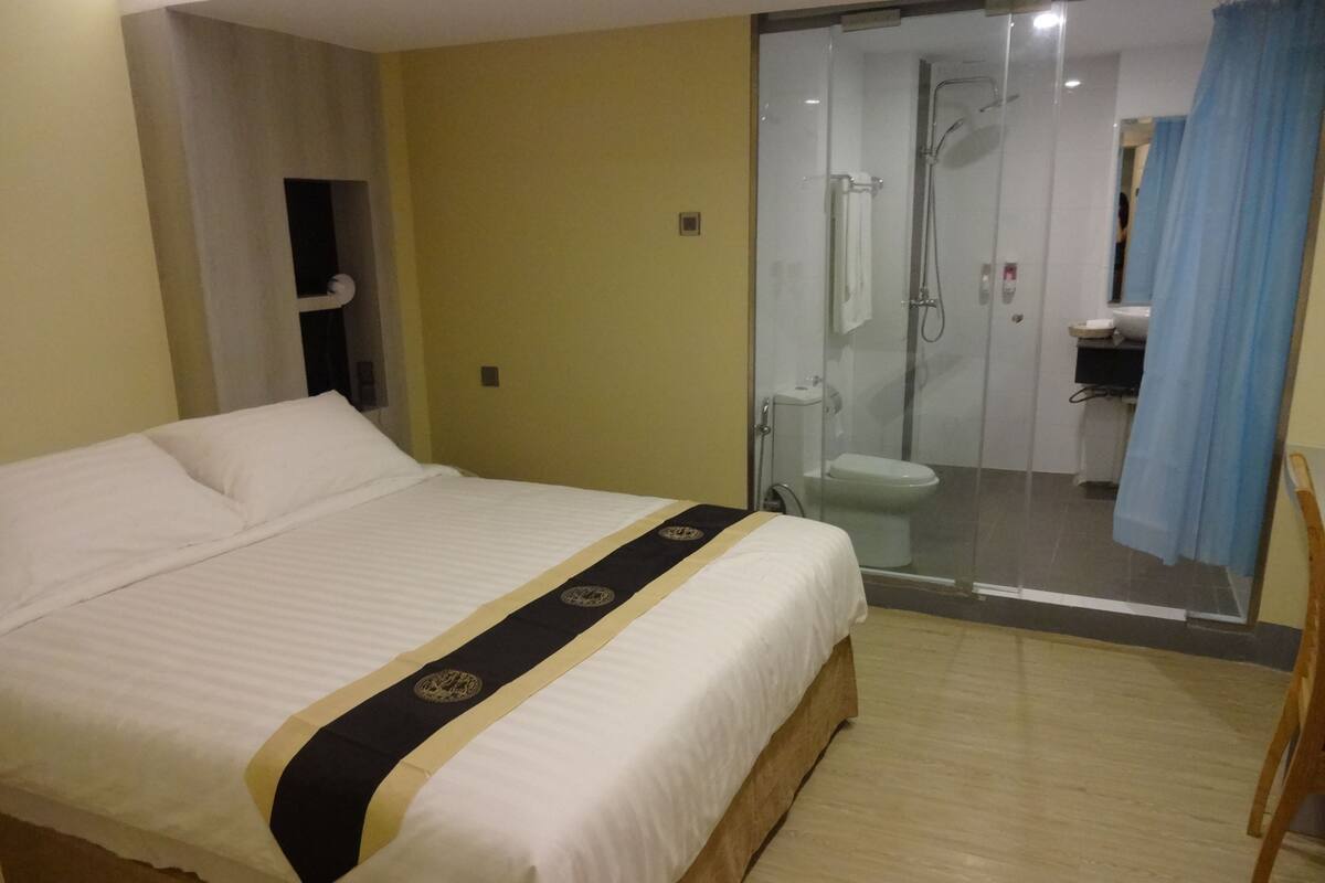A hotel room with a bed, a bathroom with a glass shower enclosure, and a visible toilet.
