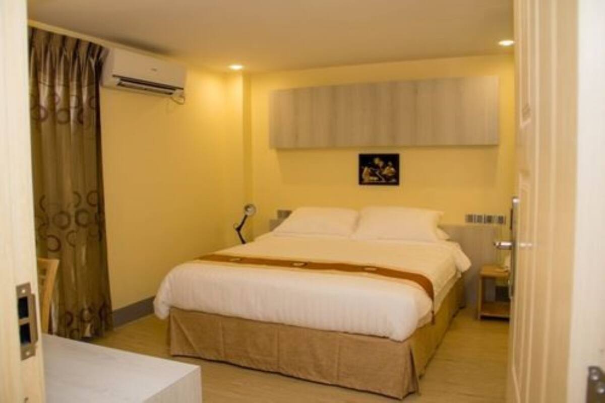 A hotel room with a bed, a bedside table, an air conditioning unit, a wall-mounted artwork, and a curtain.