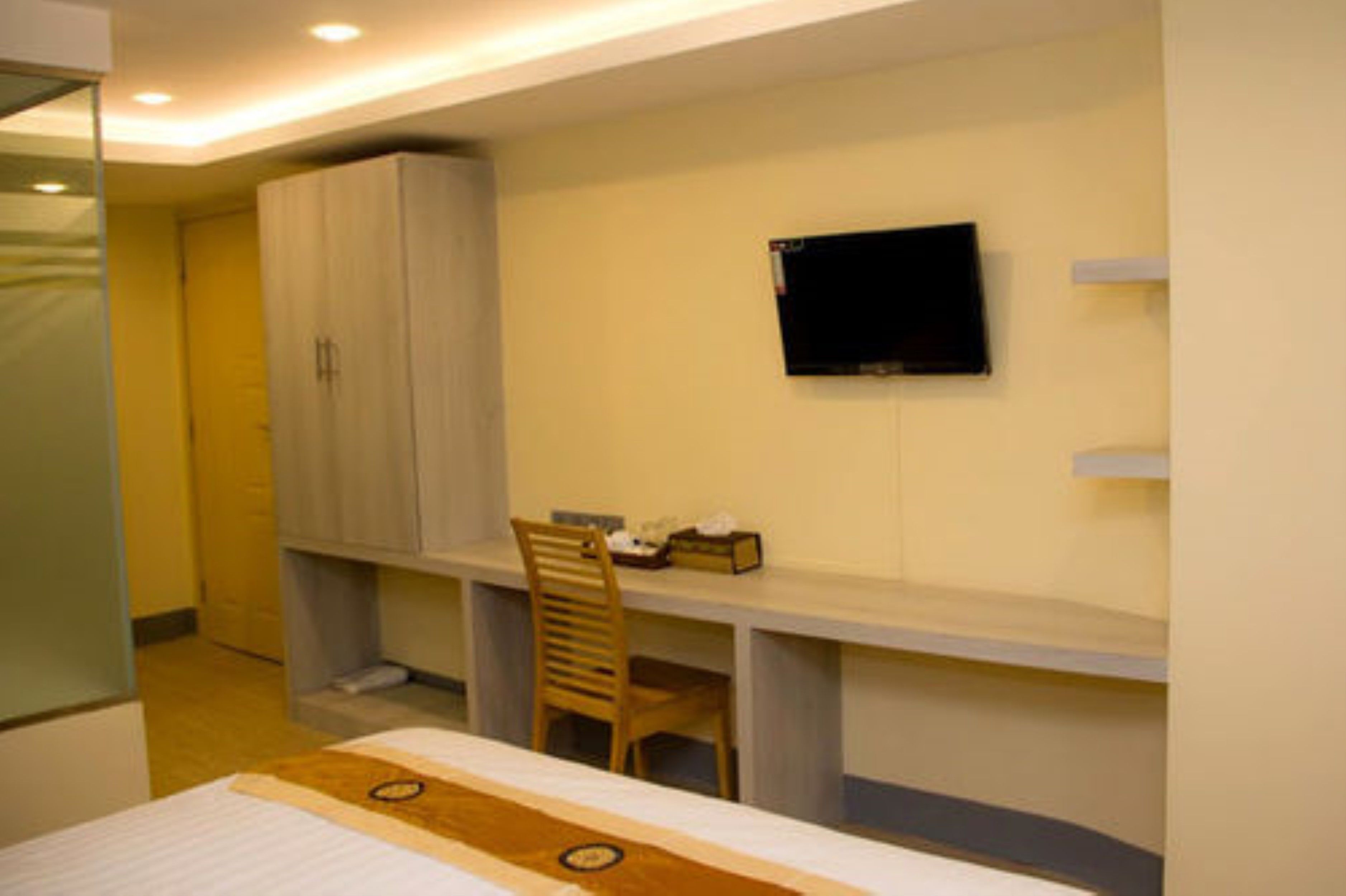 A bedroom with a bed, a desk, a chair, a wardrobe, and a TV mounted on the wall.