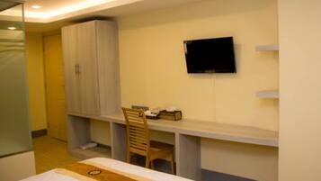 A bedroom with a bed, a desk, a chair, a wardrobe, and a TV mounted on the wall.