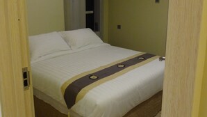 Ein Einzelbett mit braunem Schutzrock, weißer Decke und einer dekorativen Wolldecke.