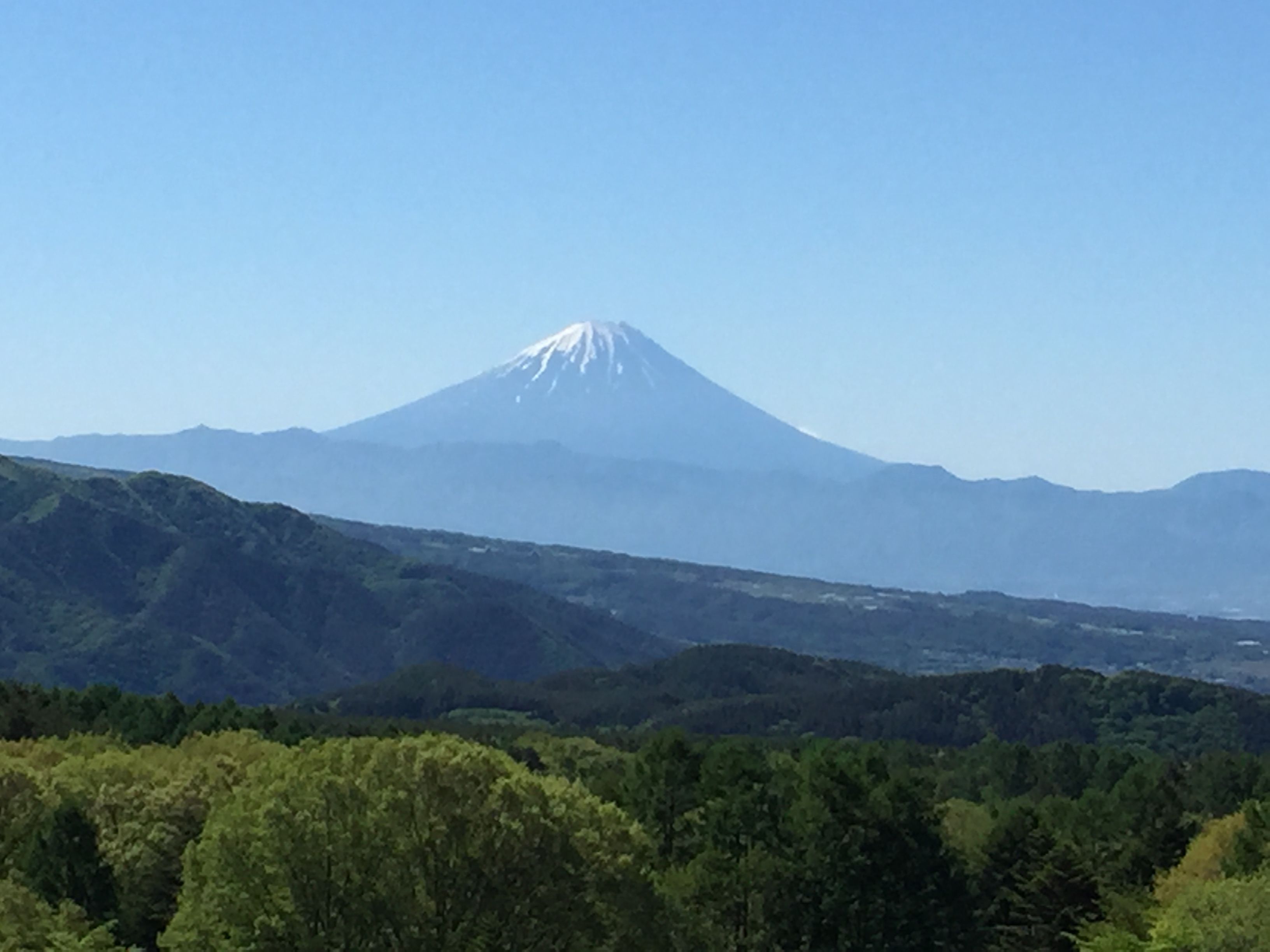 A mountain with a snow-capped peak, surrounded by forested hills.